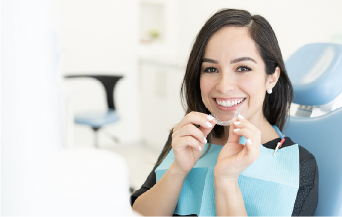 A girl with dental aligners smiling while sitting in a dentist chair 