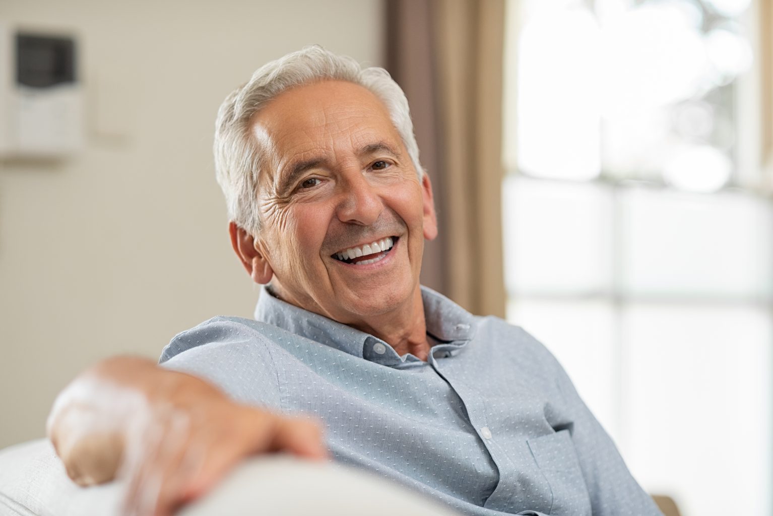 Senior man with dentures relaxing on sofa and looking at camera.