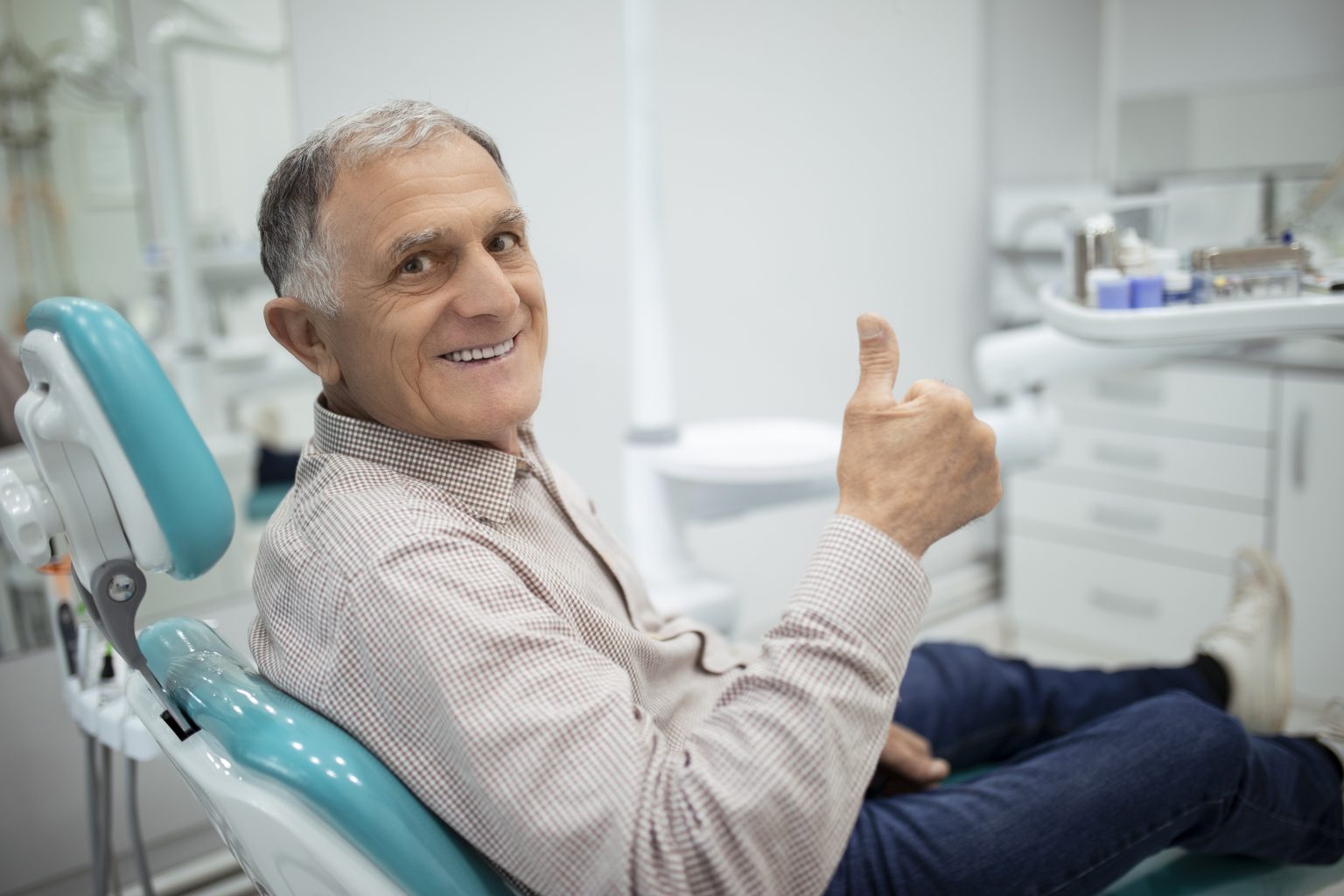older man smiling in a dentist's chair while giving a thumbs up