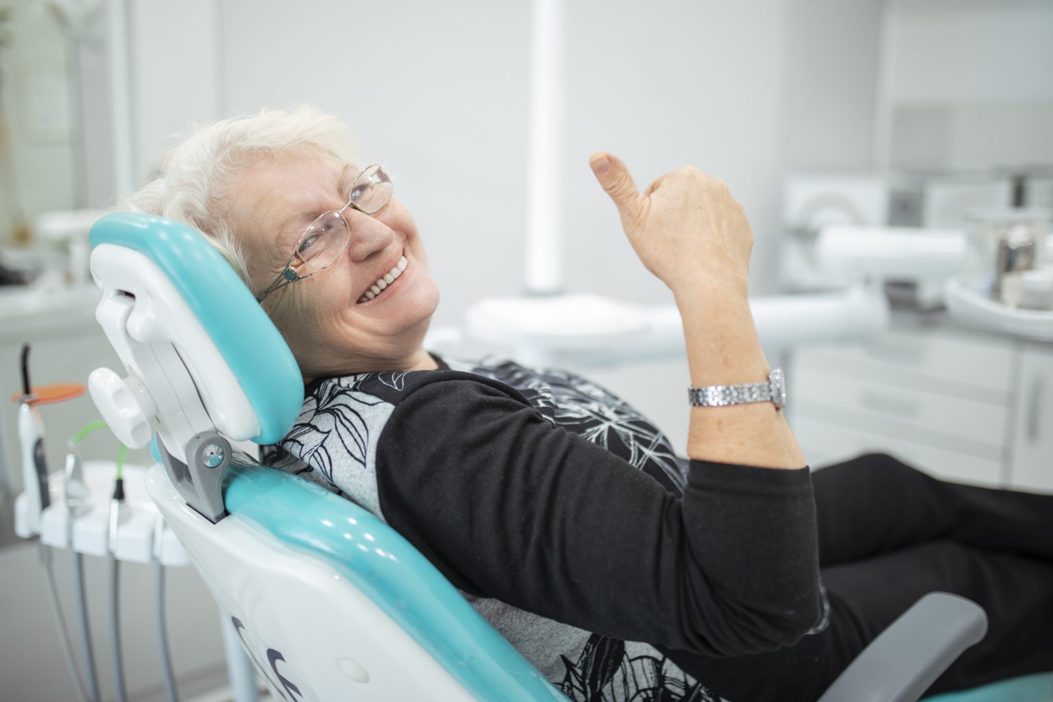 Old senior woman sitting in a dental chair thumb up