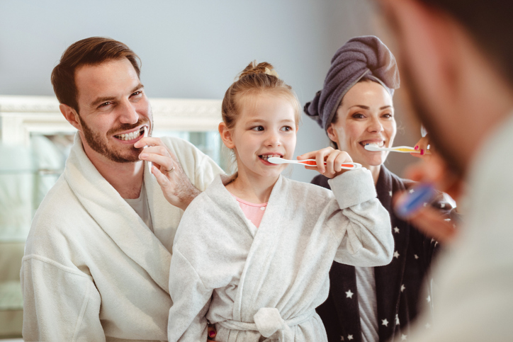 Father, mother, and daughter brushing teeth in bathroom.