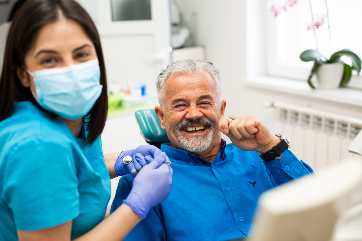 Male dental restoration patient in dental chair and dental assistant.