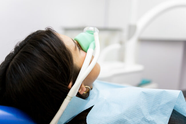 An adult woman sits in a dentist’s clinic wearing a nasal mask to inhale nitrous oxide. Dentist fear concept. Feeling of relaxation with laughing gas.
